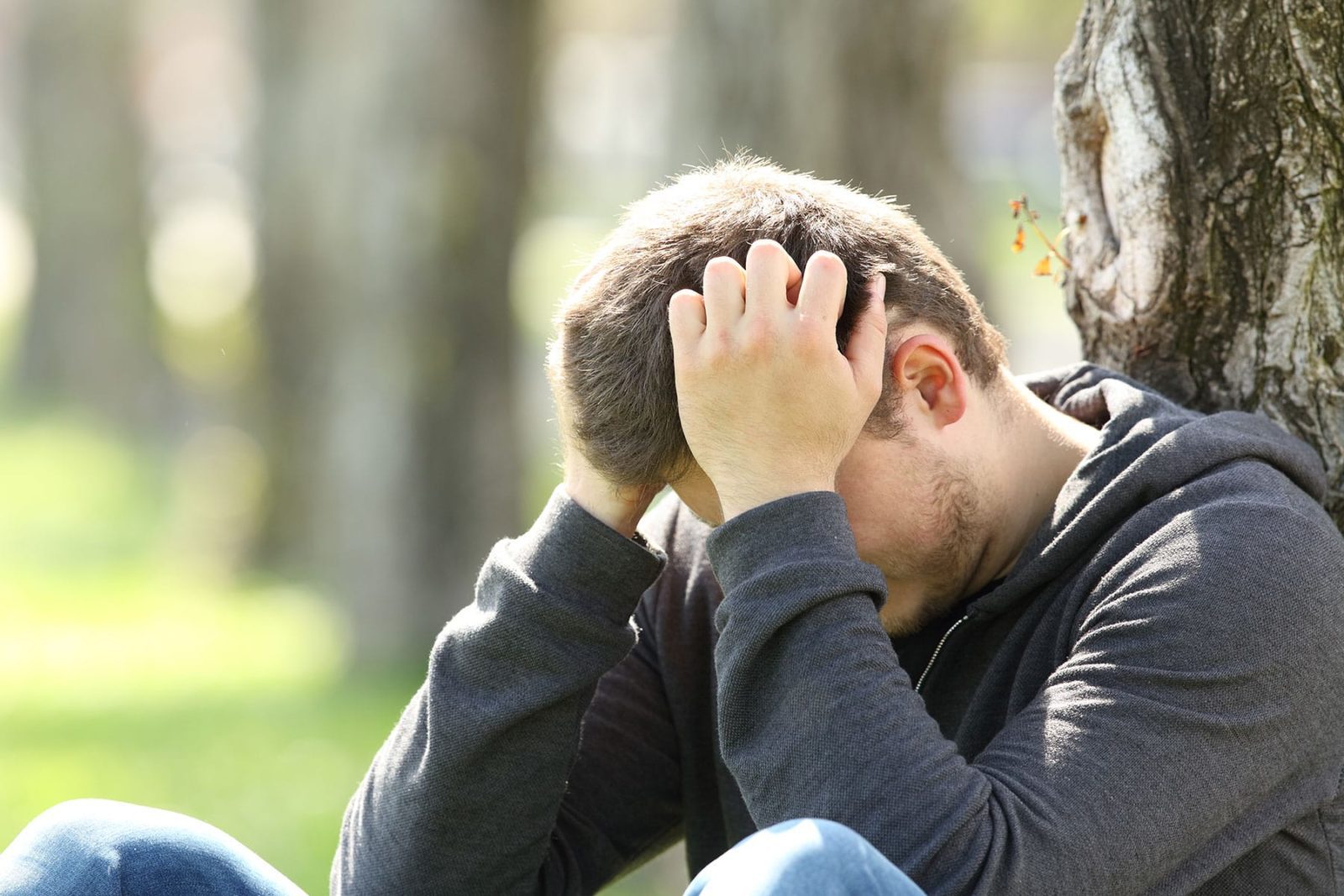 Man sat with head in hands against a tree grieving the loss of his mother