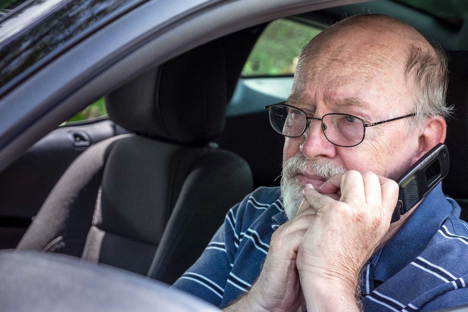 Elderly worried man sat in a car talking on a phone