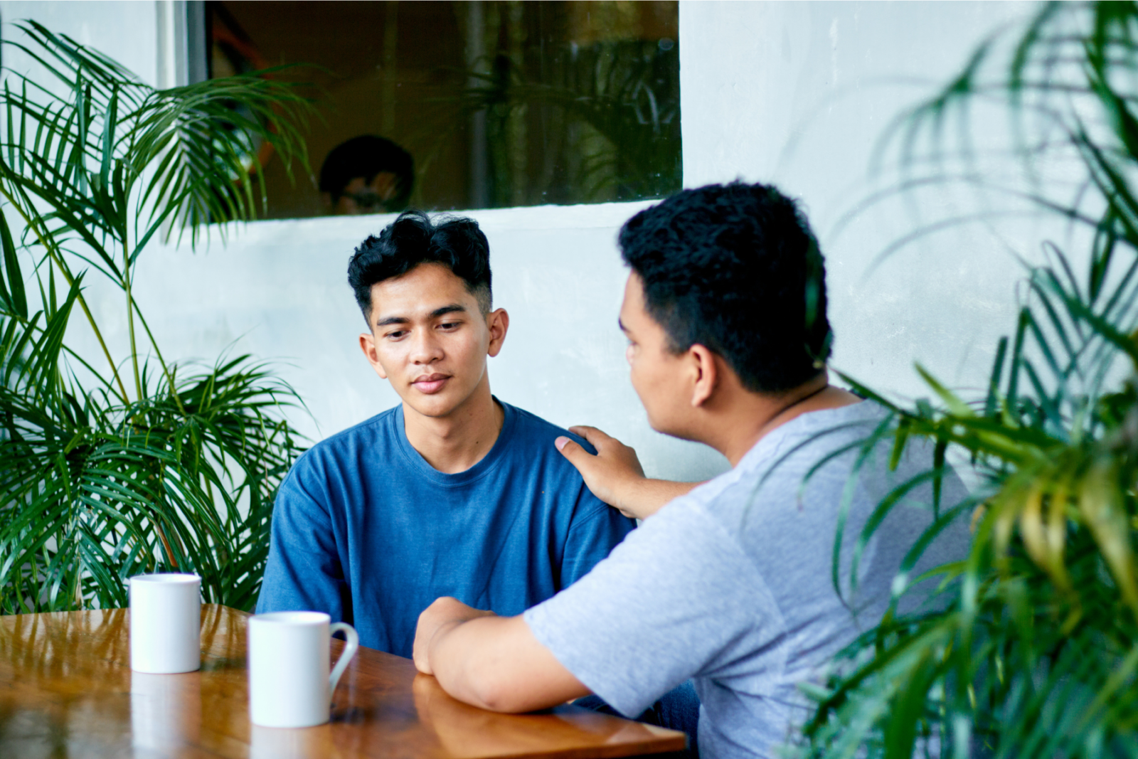 Two men in a conversation, one reaching out to the other with his hand on his shoulder
