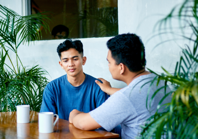 Two men in a conversation, one reaching out to the other with his hand on his shoulder
