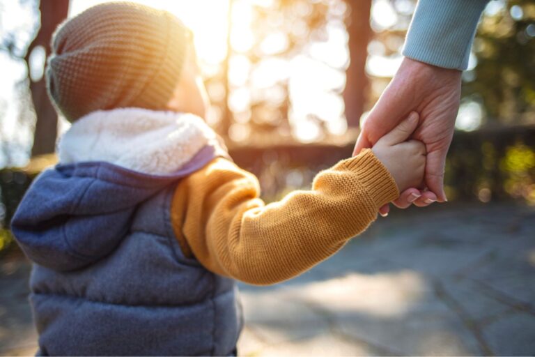 Young child and adult holding hands outside looking at the trees